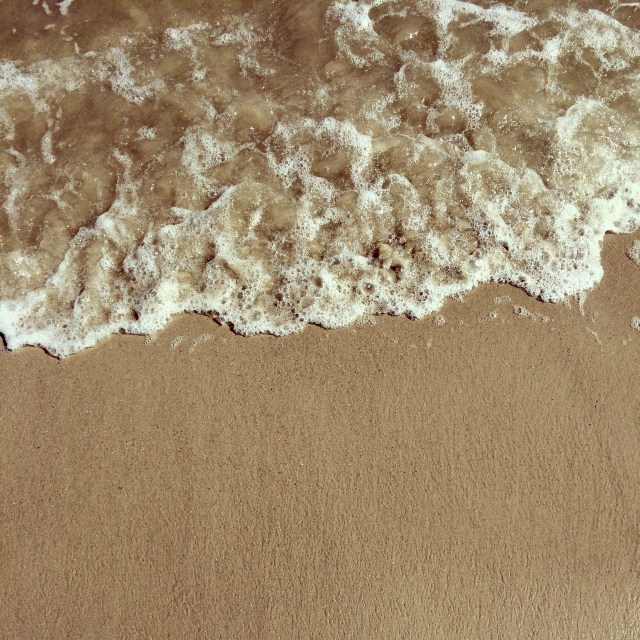 Foamy sea water rushed onto tan, brown sand.