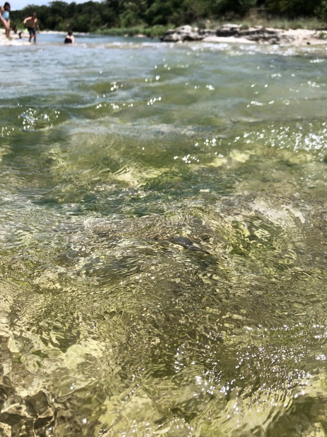 Tan riverbed is exposed under clear, moving water.
